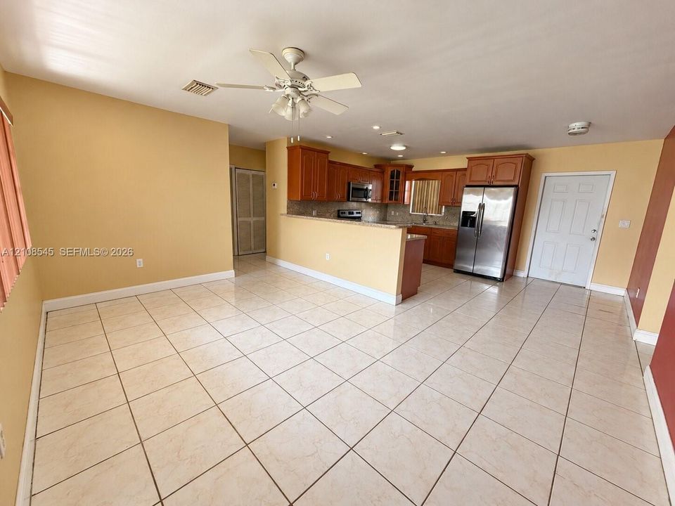 Open-concept area featuring ceramic tile flooring, recessed lighting, a ceiling fan with integrated light fixture, wood cabinetry, and stainless-steel appliances