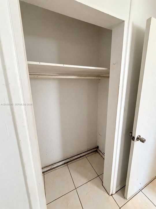 Reach-in closet featuring a built-in shelving unit, a garment rod, and ceramic tile flooring