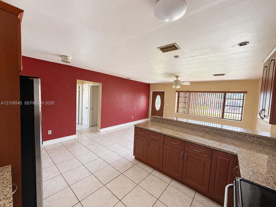 Kitchen featuring stone-finish countertops, raised-panel wood cabinetry, tile flooring, ceiling fan, and large rectangular window with horizontal blinds