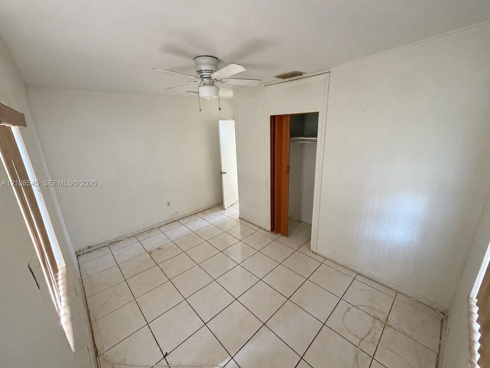 Interior space featuring white ceramic tile flooring, ceiling-mounted fan, and a built-in closet with folding doors