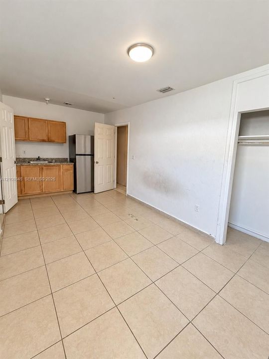 Kitchenette featuring light wood-tone cabinetry, stone-finish countertops, stainless steel refrigerator, neutral tile flooring, and built-in closet storage