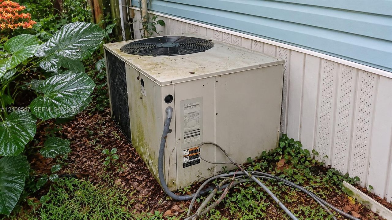 Exterior heating and cooling unit positioned against a light blue horizontal siding and vertical lattice skirting