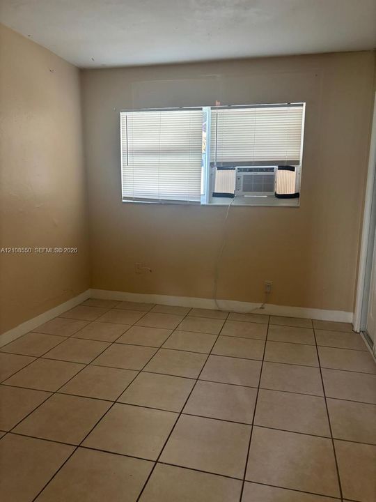 Neutral-toned interior space featuring light-colored ceramic tile flooring, a dual-pane horizontal window with integrated blinds, and painted walls