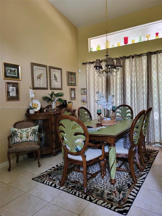 Dining area featuring vaulted ceilings, a prominent transom window, large-format tile flooring, and a multi-arm chandelier