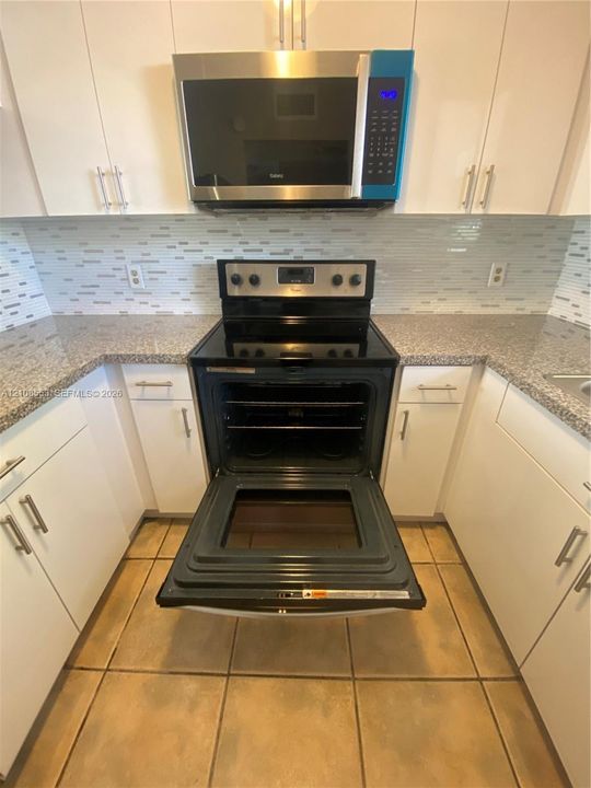 Kitchen featuring white cabinetry, stone-finish countertops, stainless steel microwave, glass-top range, and horizontal tile backsplash