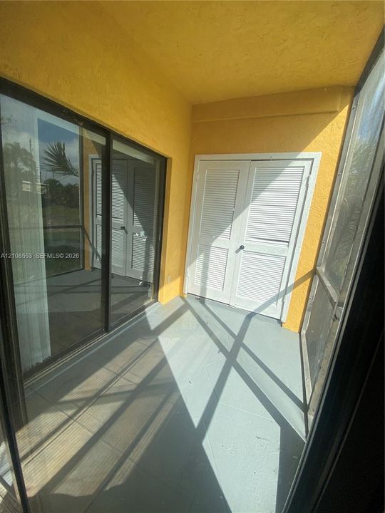 Covered patio featuring a solid-surface floor, double-door storage closet with louvered panels, and full-height glass sliding door entry