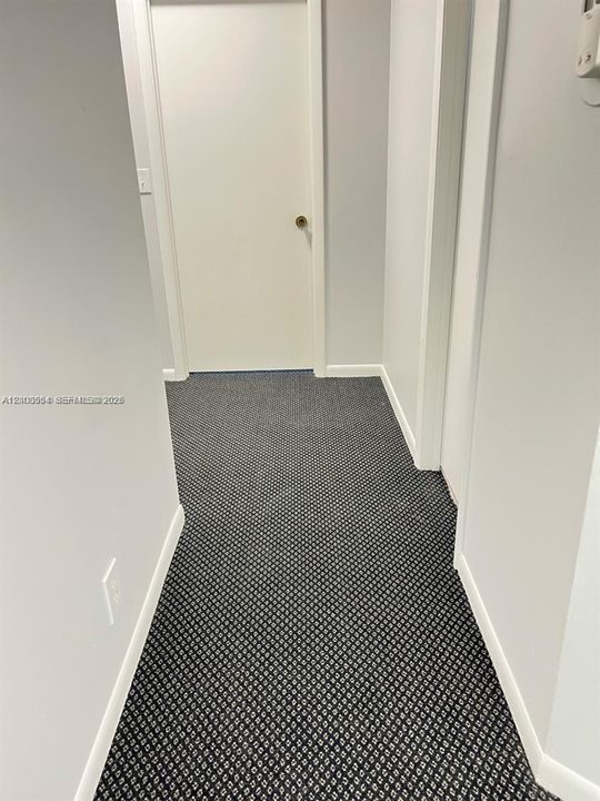 Hallway featuring neutral wall paint, geometric patterned carpeting, and a solid-core interior door with a brushed metal handle