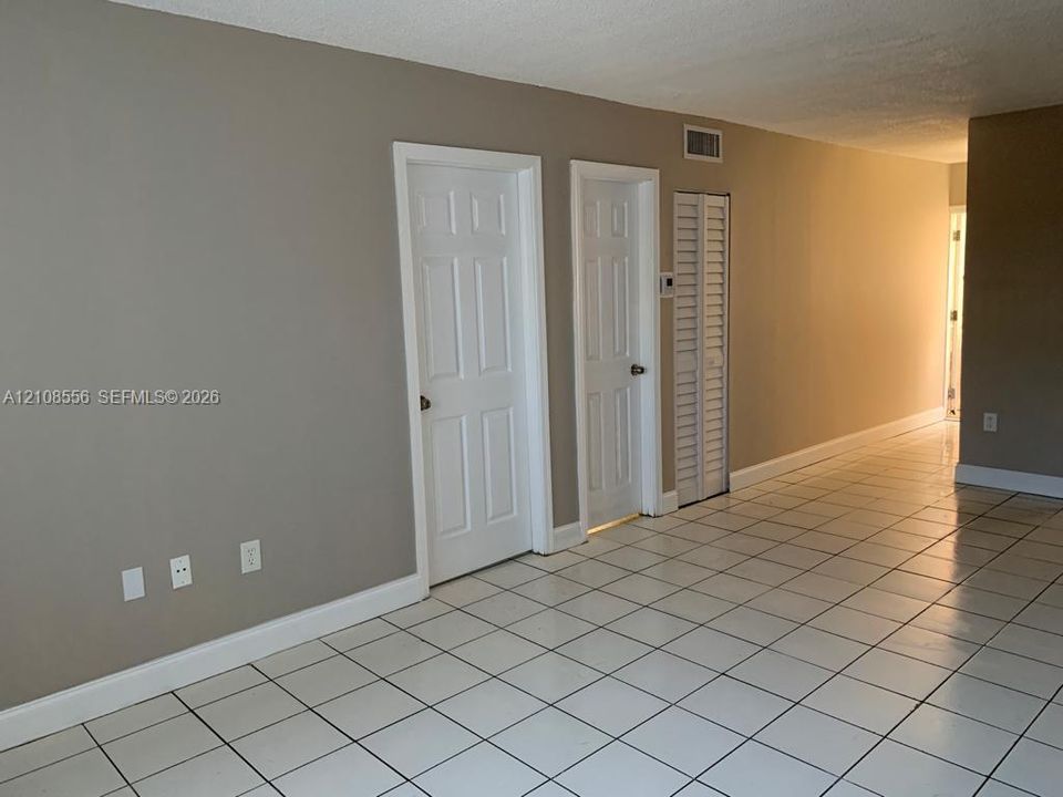 Neutral-toned interior featuring white ceramic floor tile, two interior paneled doors, and a louvered closet door