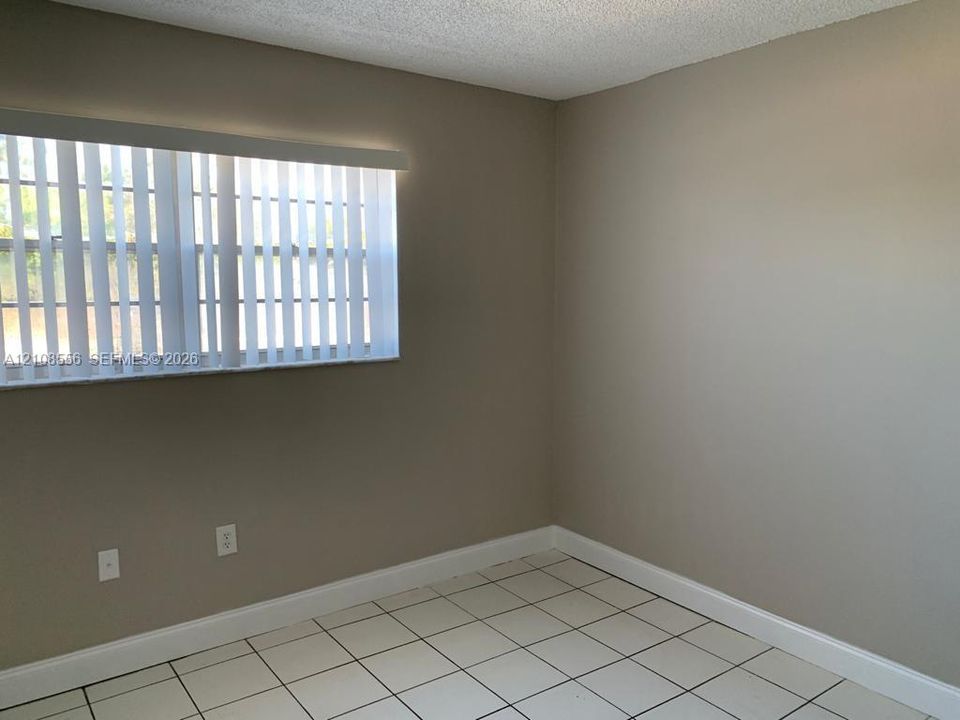Neutral-toned interior room featuring white tile flooring, vertical window blinds, and textured ceiling finish