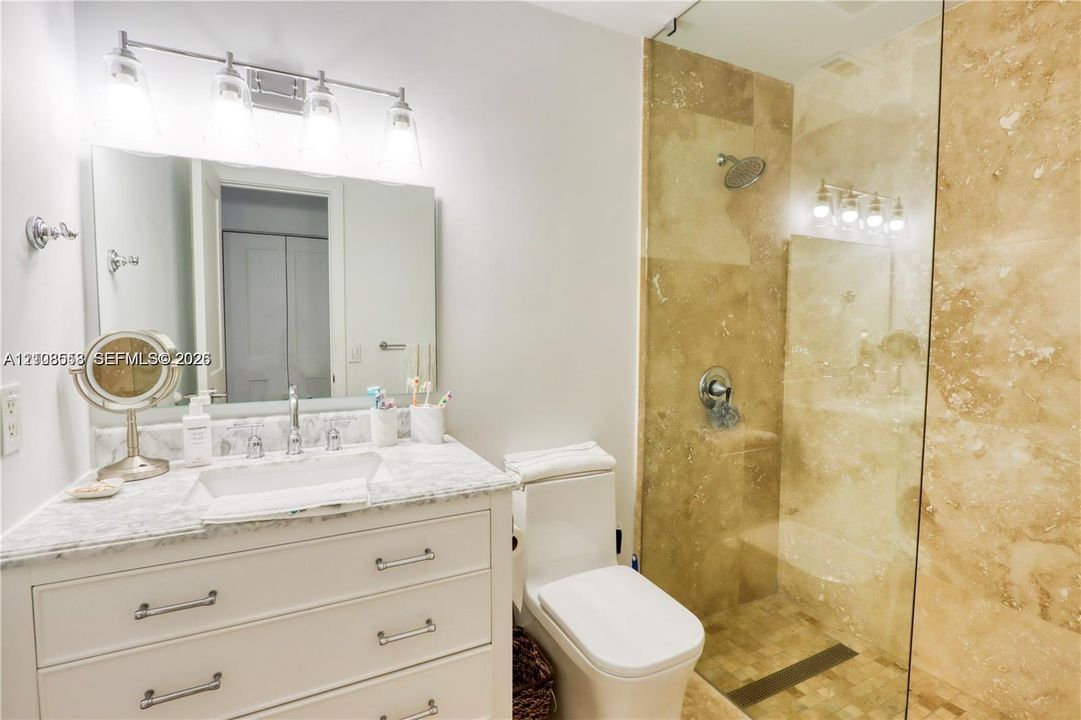 Bathroom featuring a vanity with stone countertop, undermount sink, four-light vanity fixture, and a glass-enclosed shower with tiled walls
