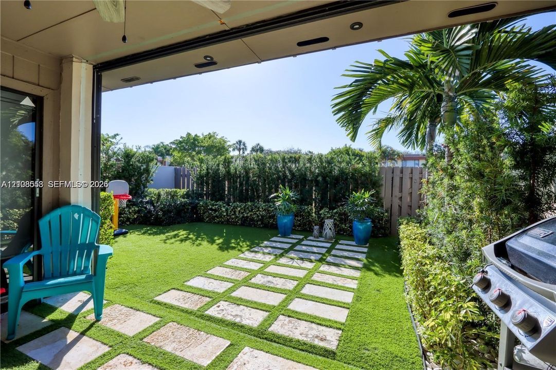 Covered patio featuring a paved walkway, synthetic turf, and perimeter privacy hedges