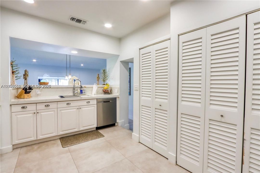 White cabinetry with metal hardware, light-colored solid surface countertops, stainless steel dishwasher, and floor-to-ceiling louvered closet doors