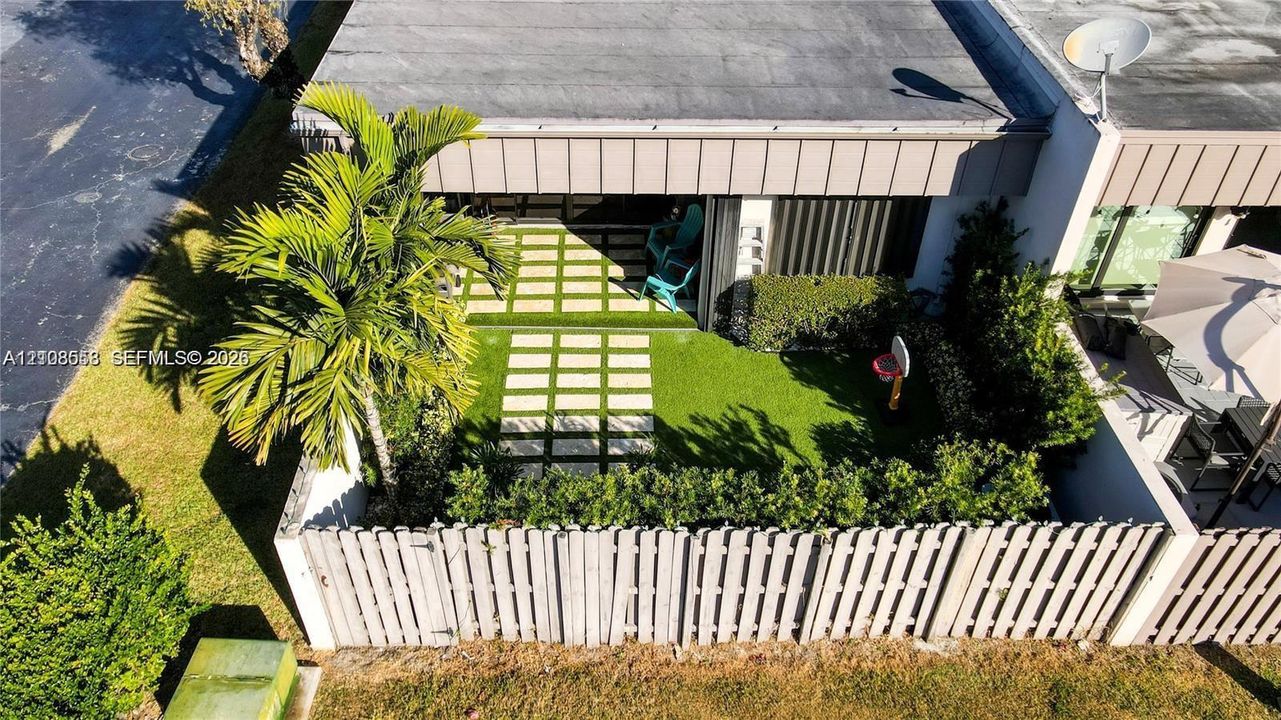 Private rear courtyard featuring a wooden privacy fence, stone paver path, manicured lawn, and palm tree landscaping