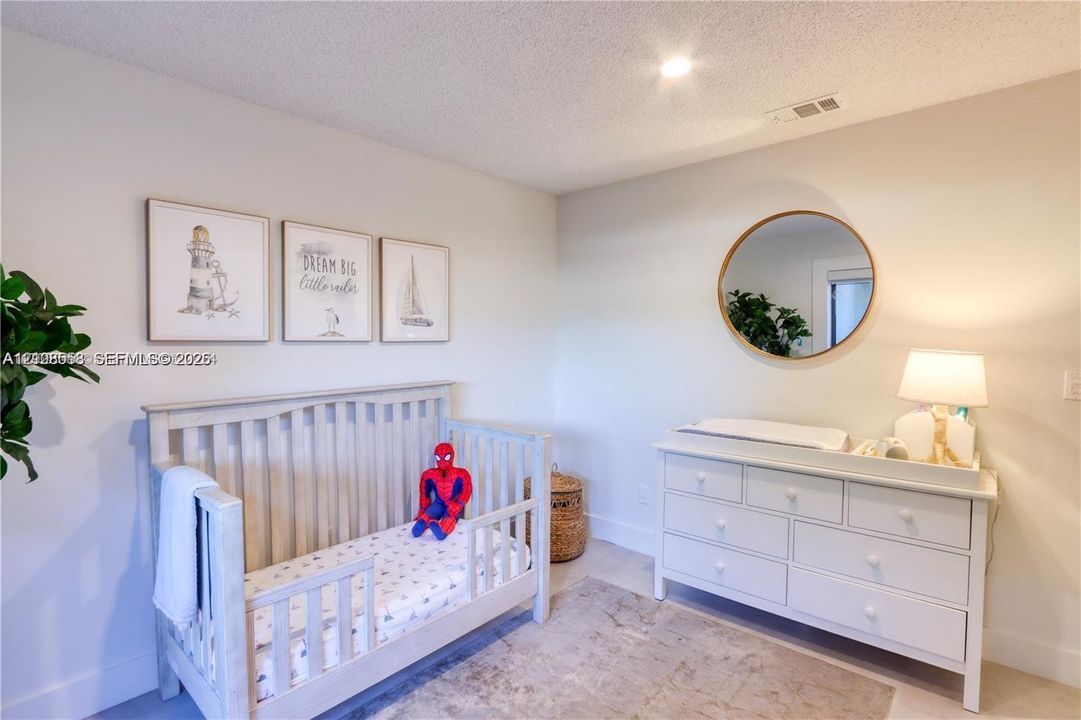 Neutral-toned interior space featuring a circular wall mirror with a metallic frame, textured ceiling, and uniform wall finishes