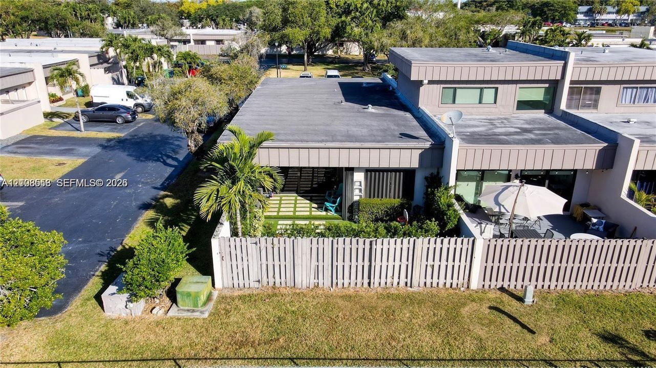 Multi-level exterior featuring a flat roofline, fenced patio area, ground-level paved terrace, and manicured landscaping