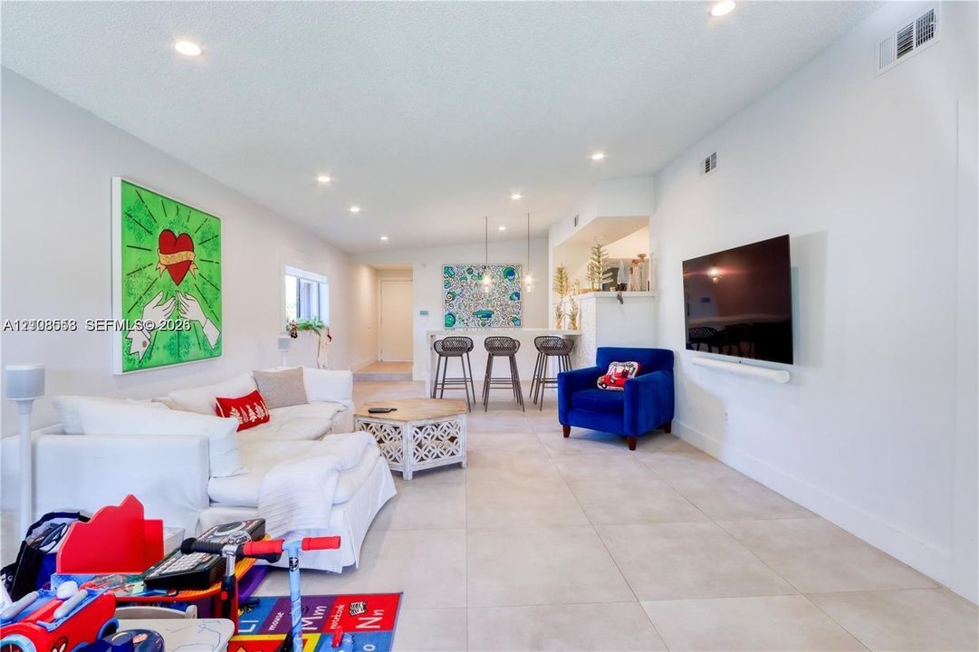 Open-concept interior featuring large-format tile flooring, recessed ceiling lighting, and a built-in kitchen breakfast bar