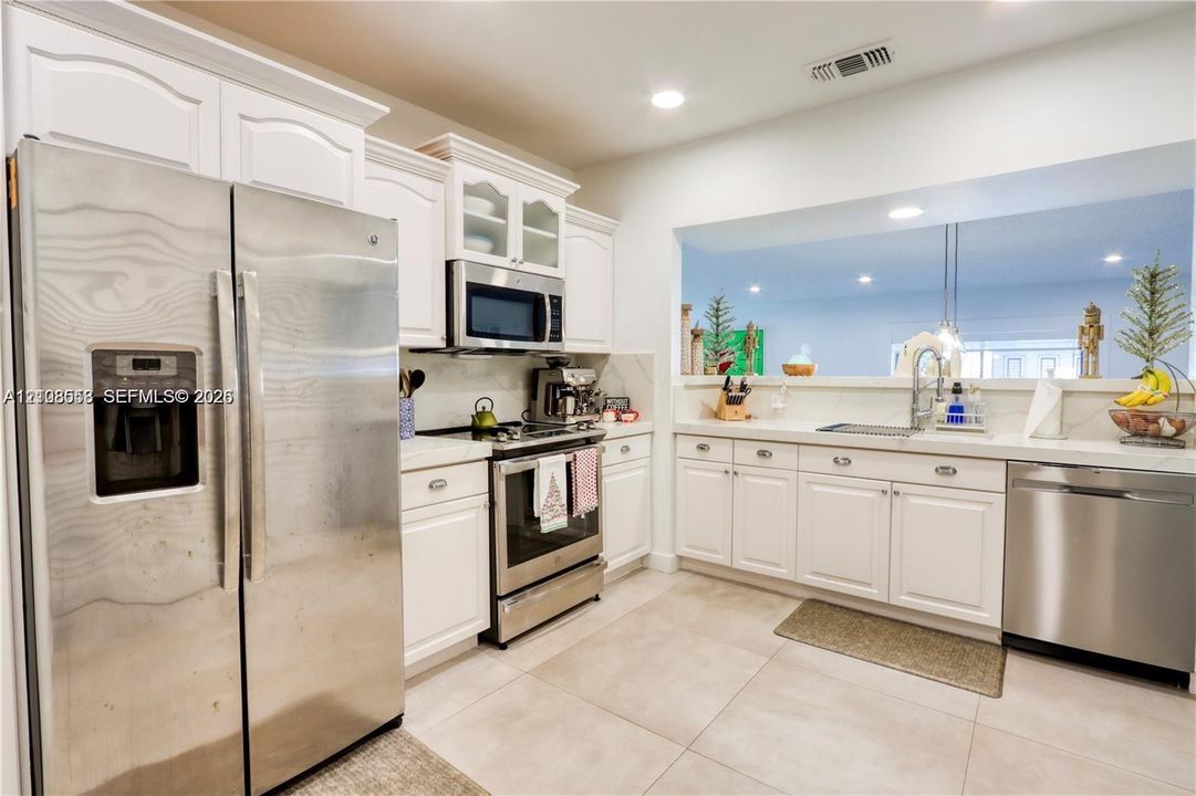Kitchen featuring white cabinetry, stainless steel appliances, neutral stone-finish countertops, and large-format tile flooring