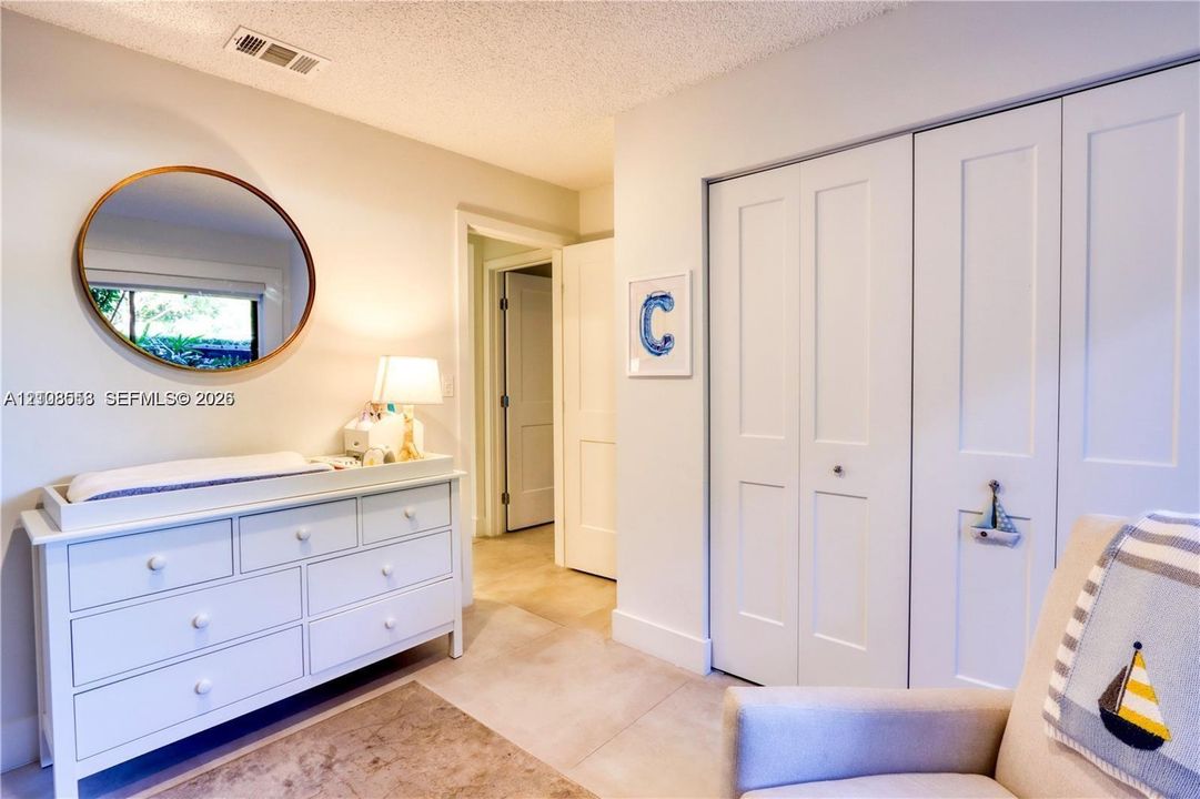 Neutral-toned interior featuring smooth-finish ceiling, large round wall mirror, and double-panel bifold closet doors
