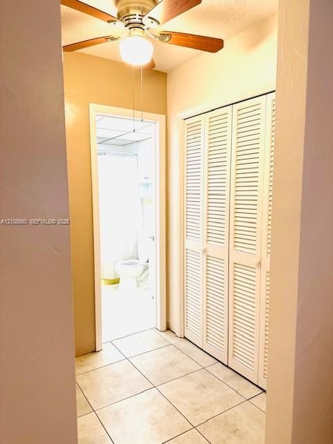 Hallway featuring tile flooring, louvered bi-fold closet doors, and a ceiling-mounted fan with integrated lighting