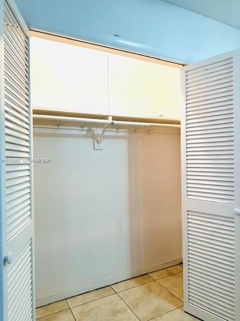 Closet featuring white louvered bi-fold doors, overhead built-in cabinetry, and tile flooring