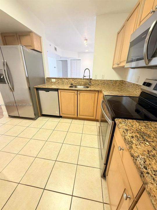 Kitchen featuring natural-finish wood cabinetry, stone-patterned countertops, stainless steel appliances, and tile flooring