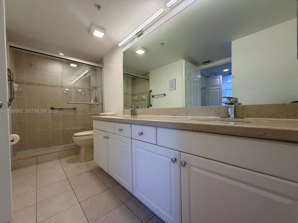 Bathroom featuring white cabinetry, stone-surface countertop, full-width wall mirror, and walk-in shower with glass enclosure