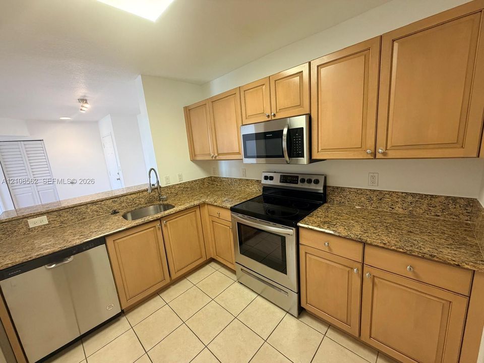 Kitchen featuring natural wood cabinetry, stone countertops, stainless steel appliances, and tile flooring