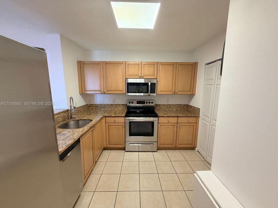 Kitchen featuring light wood cabinetry, stone-surface countertops, tile flooring, stainless steel appliances, and a recessed ceiling light