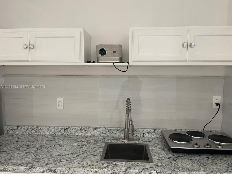 Kitchen area featuring stone-patterned countertops, a stainless steel undermount sink, a pull-down high-arch faucet, a smooth-top electric cooktop, and white cabinetry