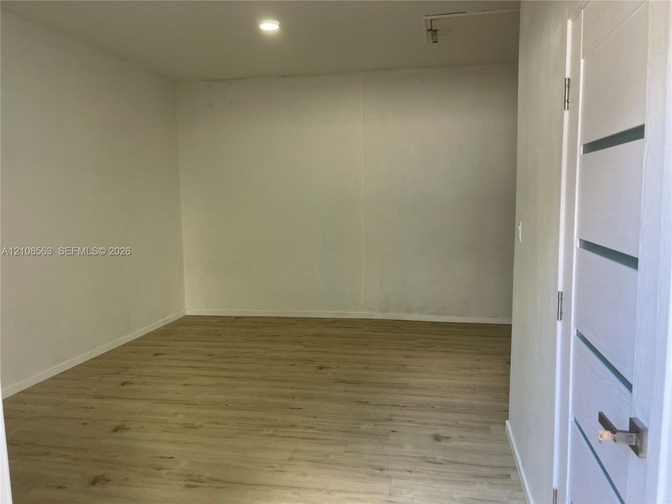 Neutral-toned interior room featuring wood-finish flooring, recessed lighting, and a modern five-panel horizontal door with a metallic handle