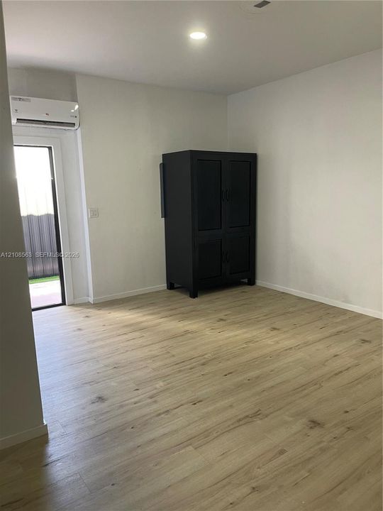 Room featuring wood-finish flooring, recessed lighting, and a wall-mounted ductless climate control unit with access to an exterior entry
