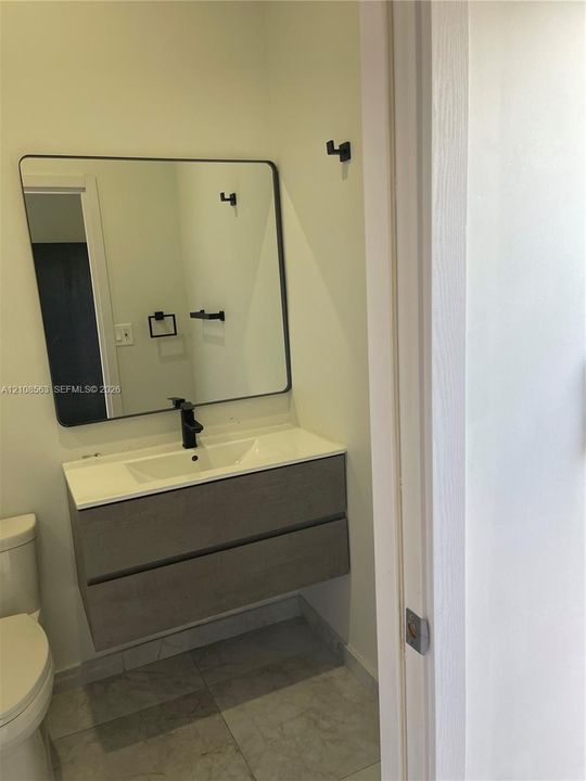 Floating dual-drawer vanity with a white integrated basin, matte black faucet, rectangular mirror with thin dark frame, and coordinating matte black wall-mounted hardware