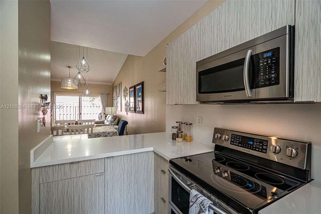 Kitchen featuring textured cabinetry, white solid-surface countertops, built-in stainless steel microwave, and stainless steel electric range
