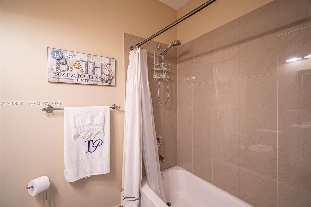 Bathtub with ceramic tile surround, integrated shower fixture, and polished metal towel bar