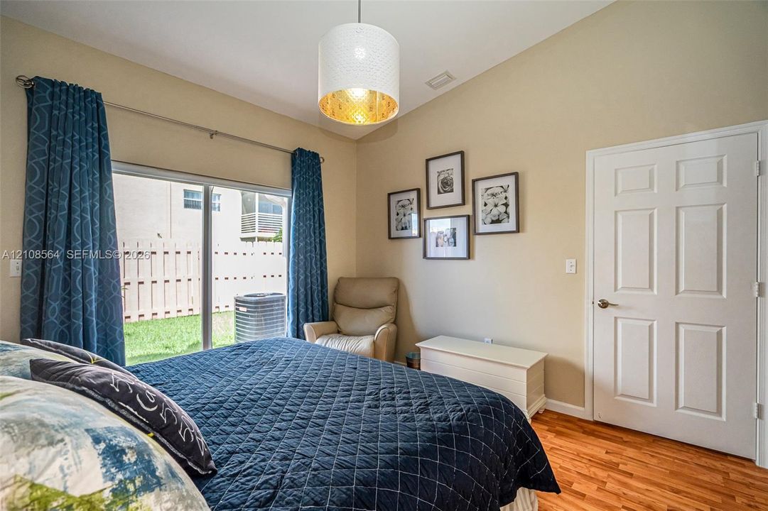 Vaulted ceilings with a drum-style pendant light, wood-finish flooring, and sliding glass doors with exterior access