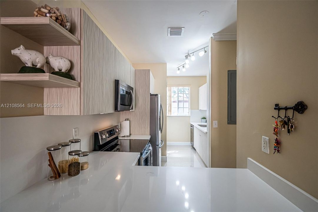 Kitchen featuring light-toned wood-finish cabinetry, quartz countertops, stainless steel appliances, open shelving, and track lighting