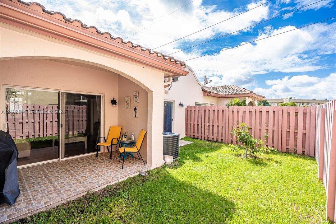 Covered patio with tile flooring, sliding glass doors, and enclosed backyard featuring a privacy fence and manicured lawn