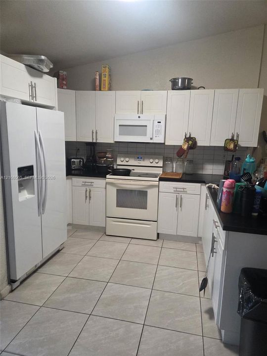 Kitchen featuring white shaker-style cabinetry, dark solid-surface countertops, white tile backsplash, and ceramic floor tiling