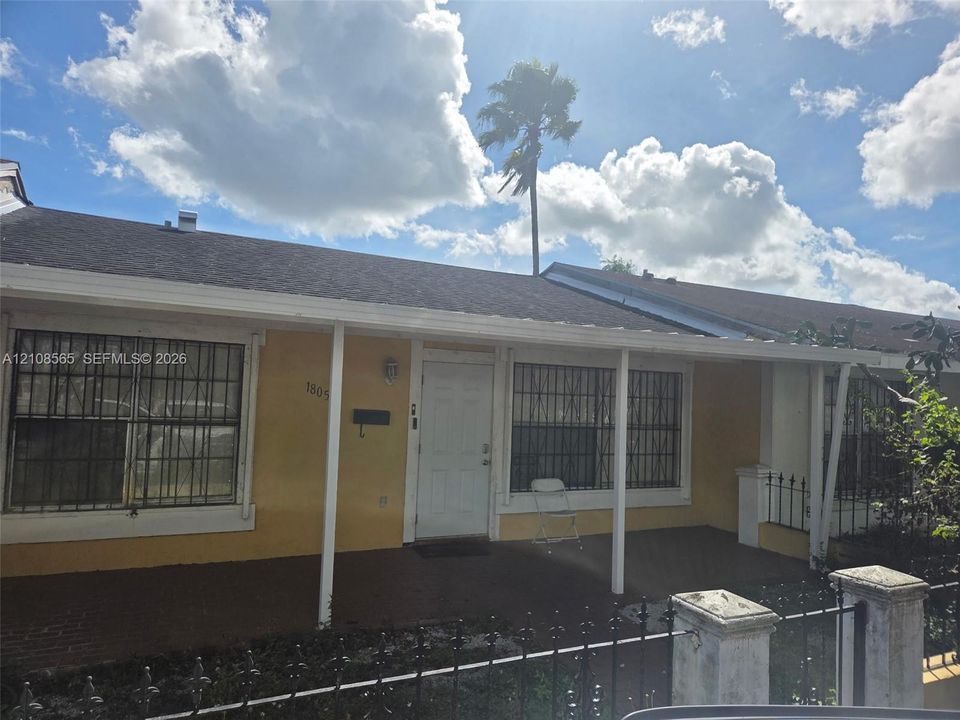 Single-story residence featuring a covered front porch, exterior metal window security bars, a concrete front patio, and a perimeter metal fence with masonry pillars