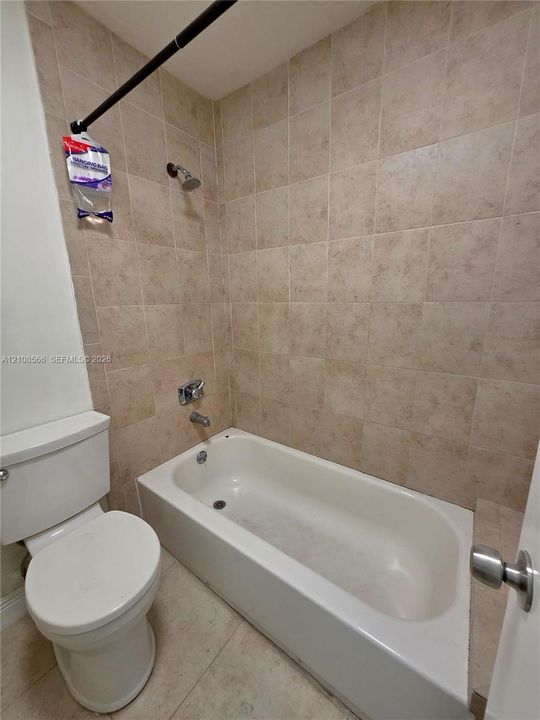 Full-sized bathtub with tile surround, porcelain toilet, and chrome-finished plumbing fixtures