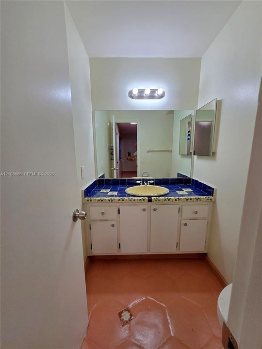 Vanity featuring white cabinetry, blue tiled countertop, integrated rounded sink, full-width mirror, and three-light fixture