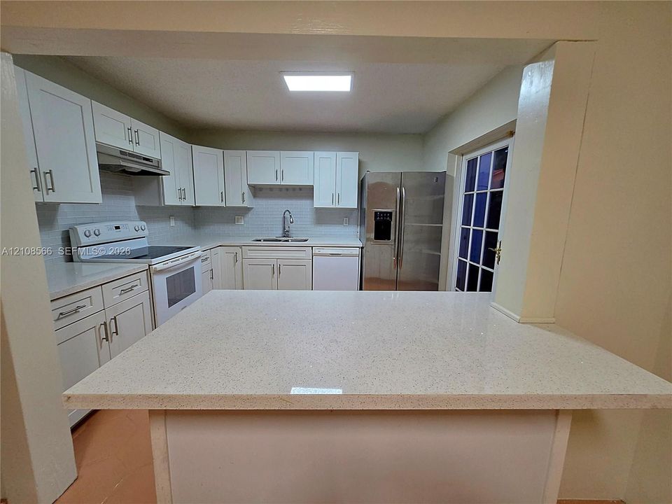 Kitchen featuring a peninsula with a quartz countertop, white cabinetry, a white subway tile backsplash, and stainless steel appliances