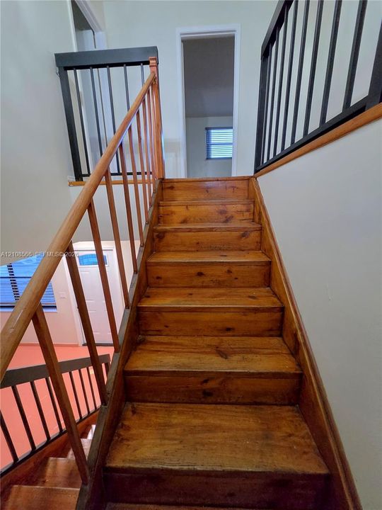 Staircase featuring wood-finish treads, a handrail with wood spindles, and a matte black metal balustrade
