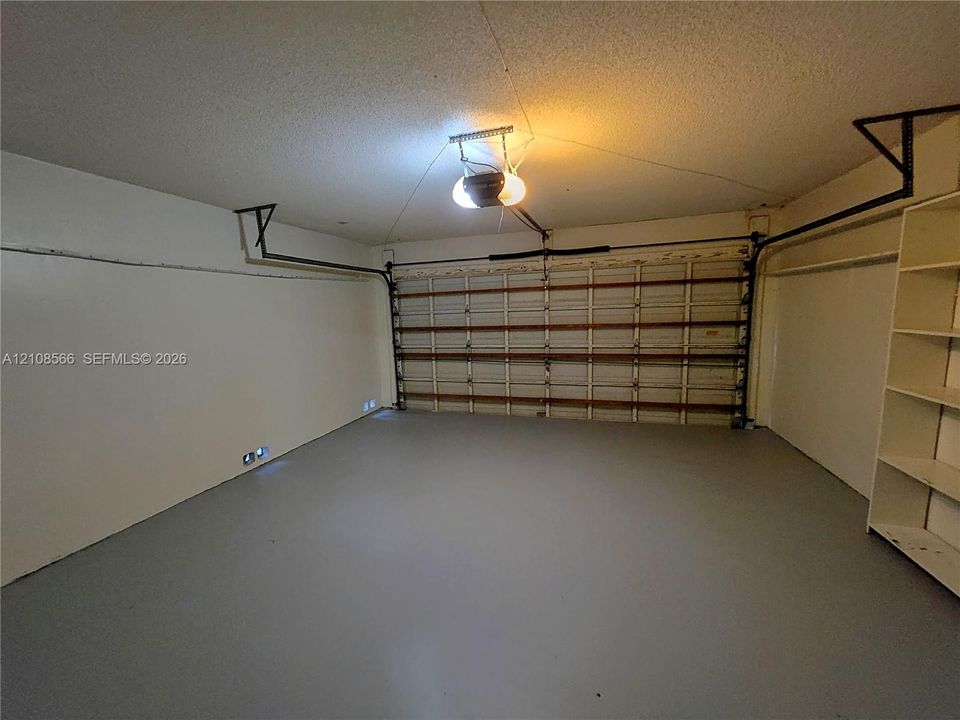 Enclosed garage featuring painted concrete flooring, a horizontal paneled overhead door, an automated door opener, and built-in shelving