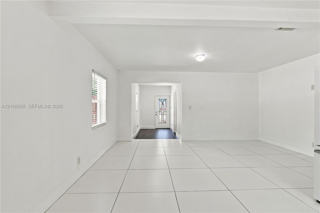 Large-format white tile flooring, ceiling beam detail, white wall finishes, and exterior door with glass detailing