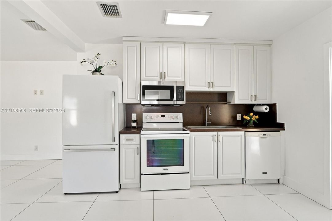 Kitchen featuring white cabinetry, solid-surface countertops, integrated stainless steel microwave, large-format tile flooring, and stainless steel faucet hardware