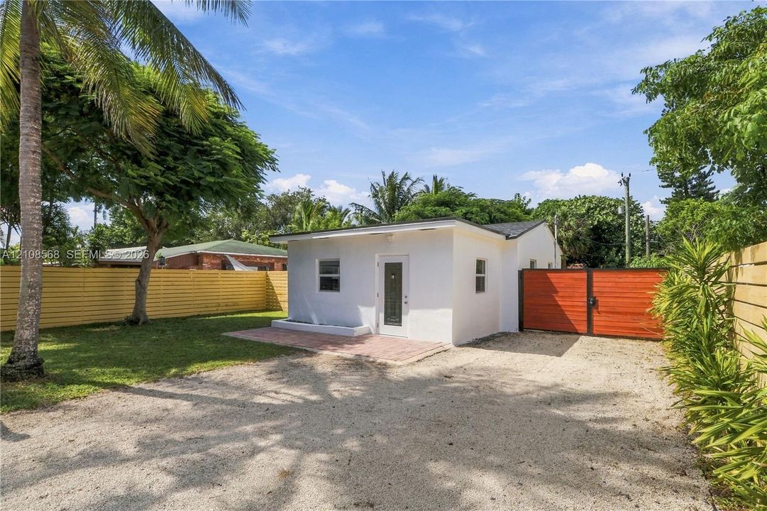 Detached structure featuring a crisp white exterior, a brick-paver patio, a gravel surface, and enclosed horizontal slat fencing