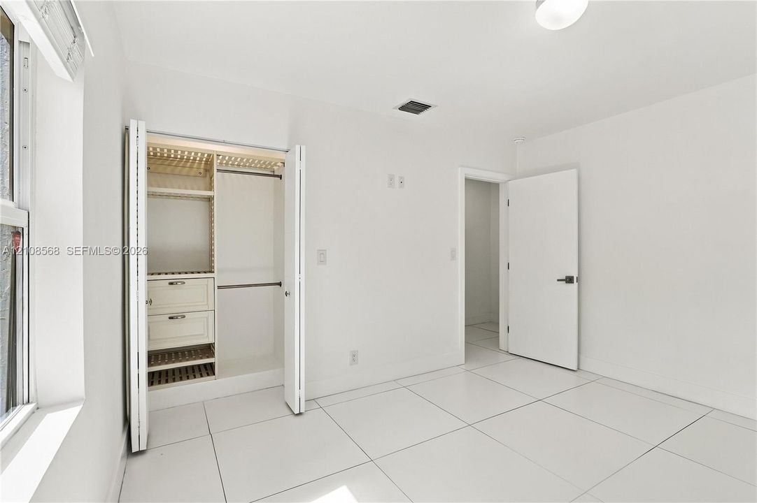 Interior space featuring white tile flooring, neutral walls, and a closet with custom built-in shelving and integrated drawer storage
