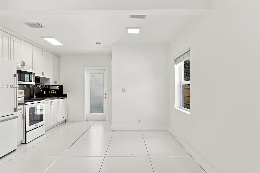 Kitchen featuring white shaker-style cabinetry, dark stone-finish countertops, tile flooring, and integrated white appliances