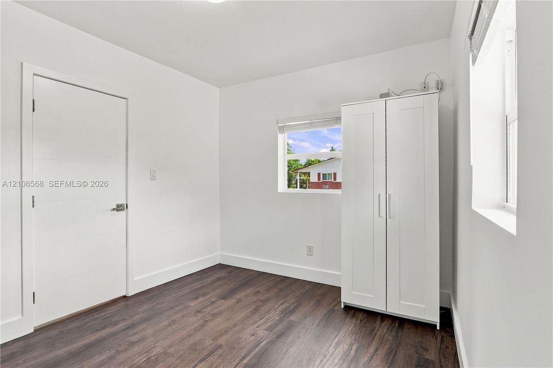 Neutral-toned room featuring wood-finish flooring, white walls, horizontal-panel interior door, and multiple windows